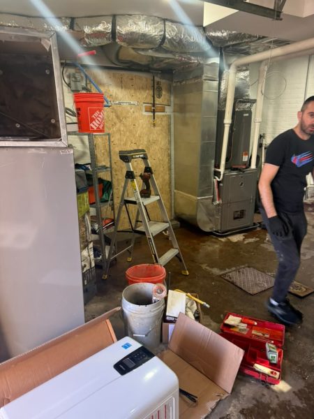 A technician with equipment in a commercial basement, hoses run out across the floor.