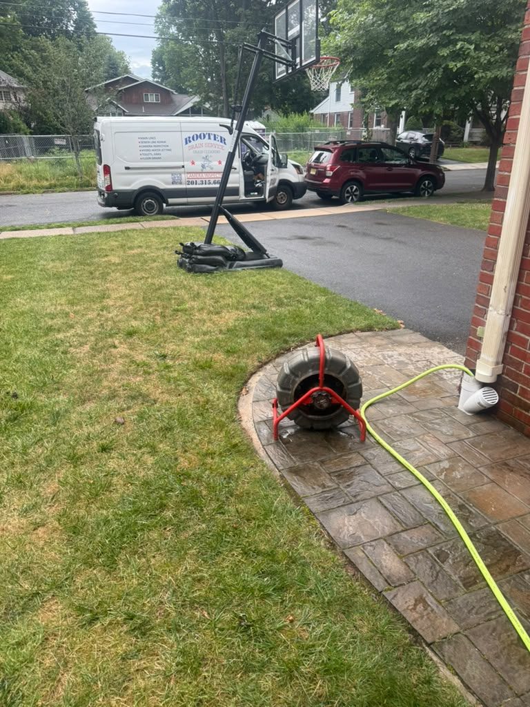 The hose run from the van across a lawn to a cleanout beside a brick path, with the drain machine in place.