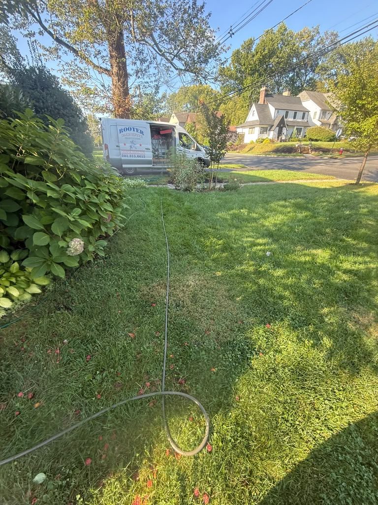 The hose run down a lawn past a hedge toward the street, with houses beyond.