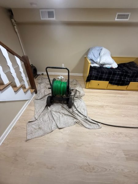 A drain machine on protective sheeting in a room, hose coiled on the floor beside it.