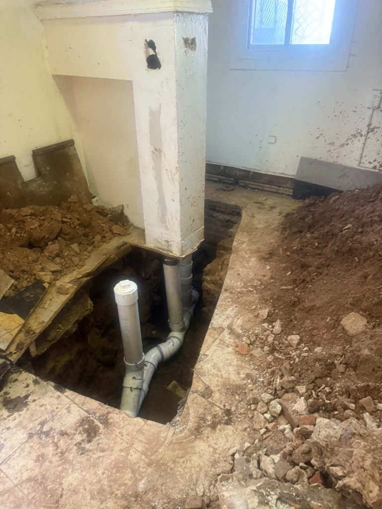 New white PVC pipework fitted into an opened section of basement floor, ready for backfilling.