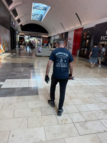 A technician in a Rooter Drain Service shirt walking through a tiled retail arcade carrying tools.