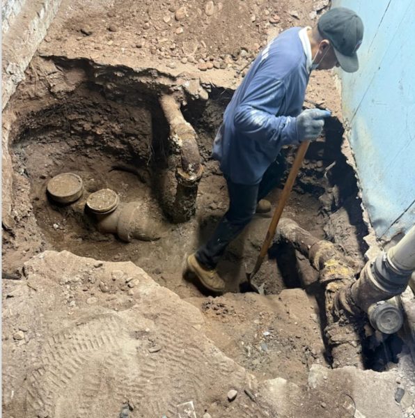 A technician standing in an open excavation, working on a pipe at the bottom of the hole.
